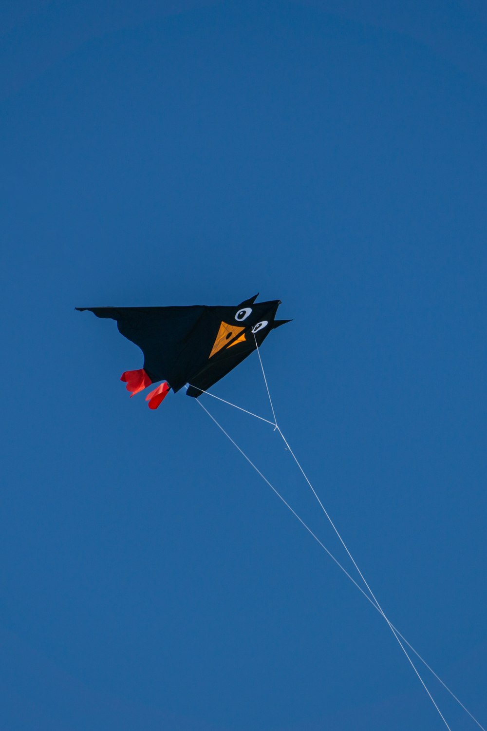 a black and yellow kite flying in a blue sky