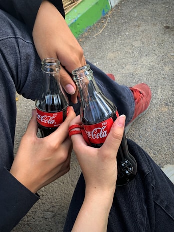 Hands holding a variety of colorful bottled drinks outdoors.