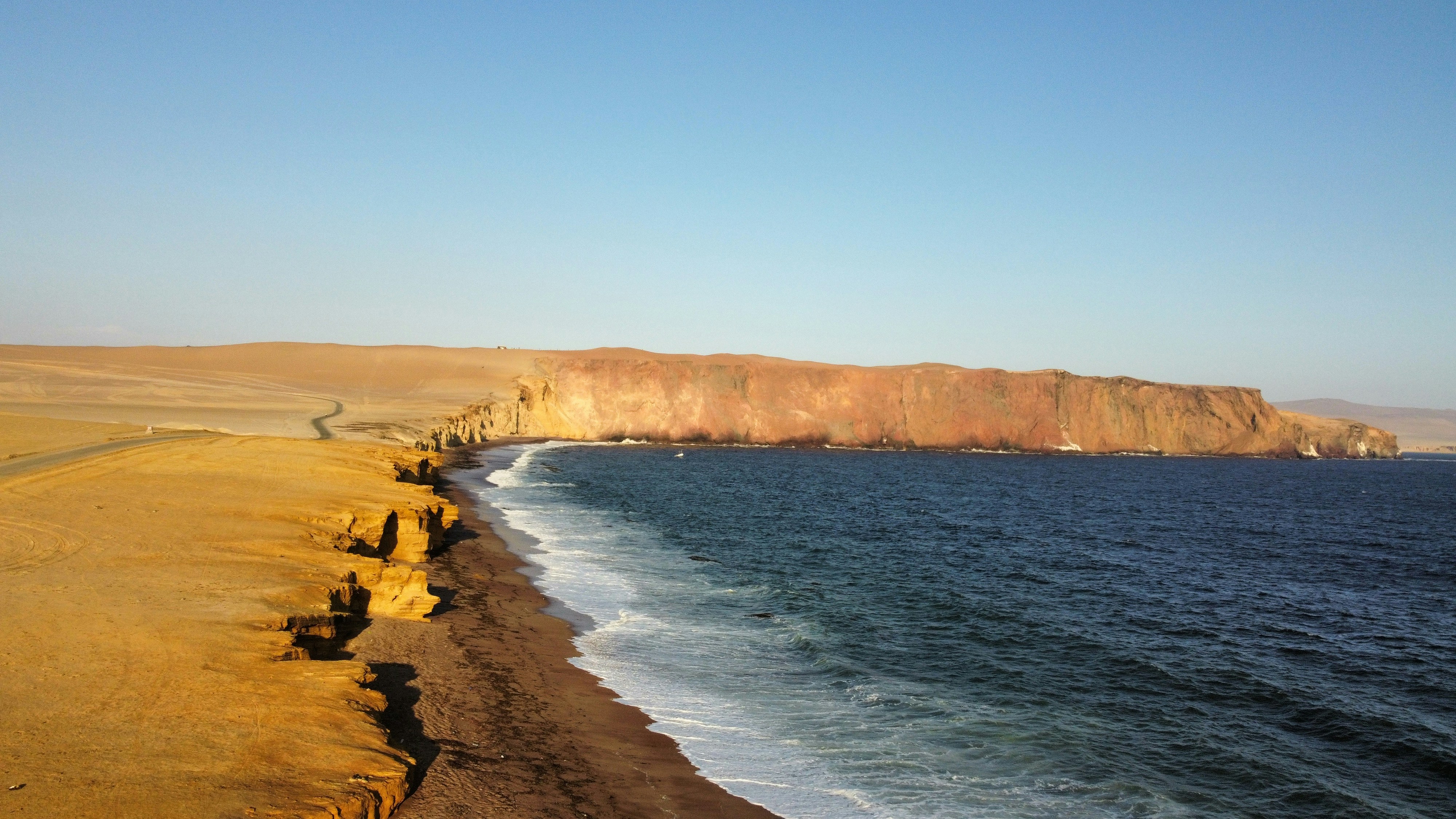 Coastal cliffs meet the ocean under a clear sky.