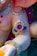 A close-up of a decorative sculpture featuring intricate jewelry designs. The sculpture has a glossy finish with embellishments of pearls and brightly colored stones, including red and blue gemstones. The jewelry includes ornate arm bands and necklaces with gold accents.