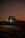 A dune buggy is captured at dusk, with its headlights glowing brightly against a backdrop of dark, rolling sand dunes. The sky is softly lit with an orange gradient, adding a sense of adventure and solitude to the scene.