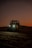 A dune buggy is captured at dusk, with its headlights glowing brightly against a backdrop of dark, rolling sand dunes. The sky is softly lit with an orange gradient, adding a sense of adventure and solitude to the scene.
