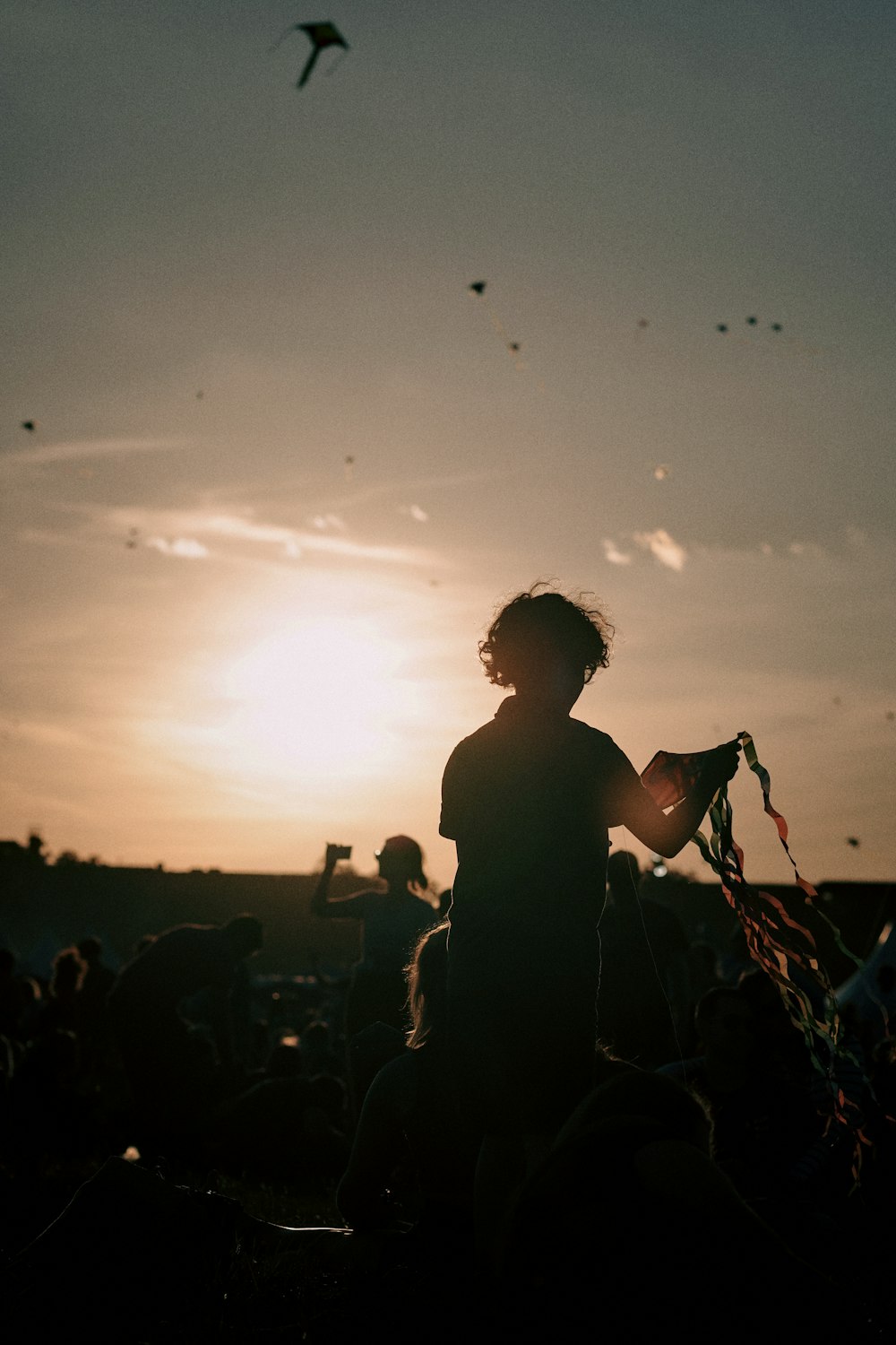 Una persona sosteniendo una cometa frente a una puesta de sol