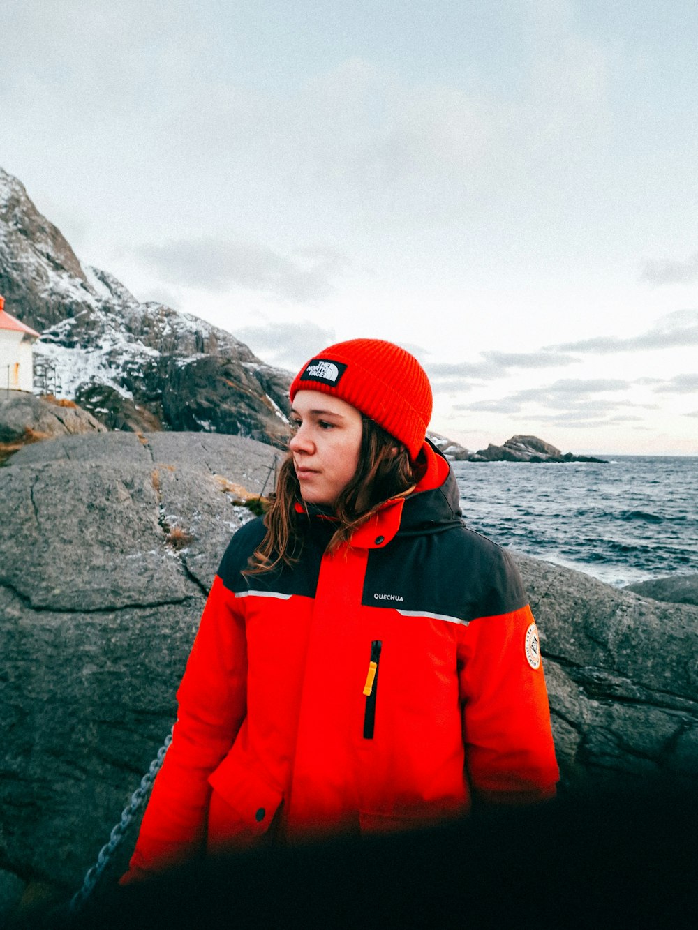 a woman in a red jacket standing by the ocean