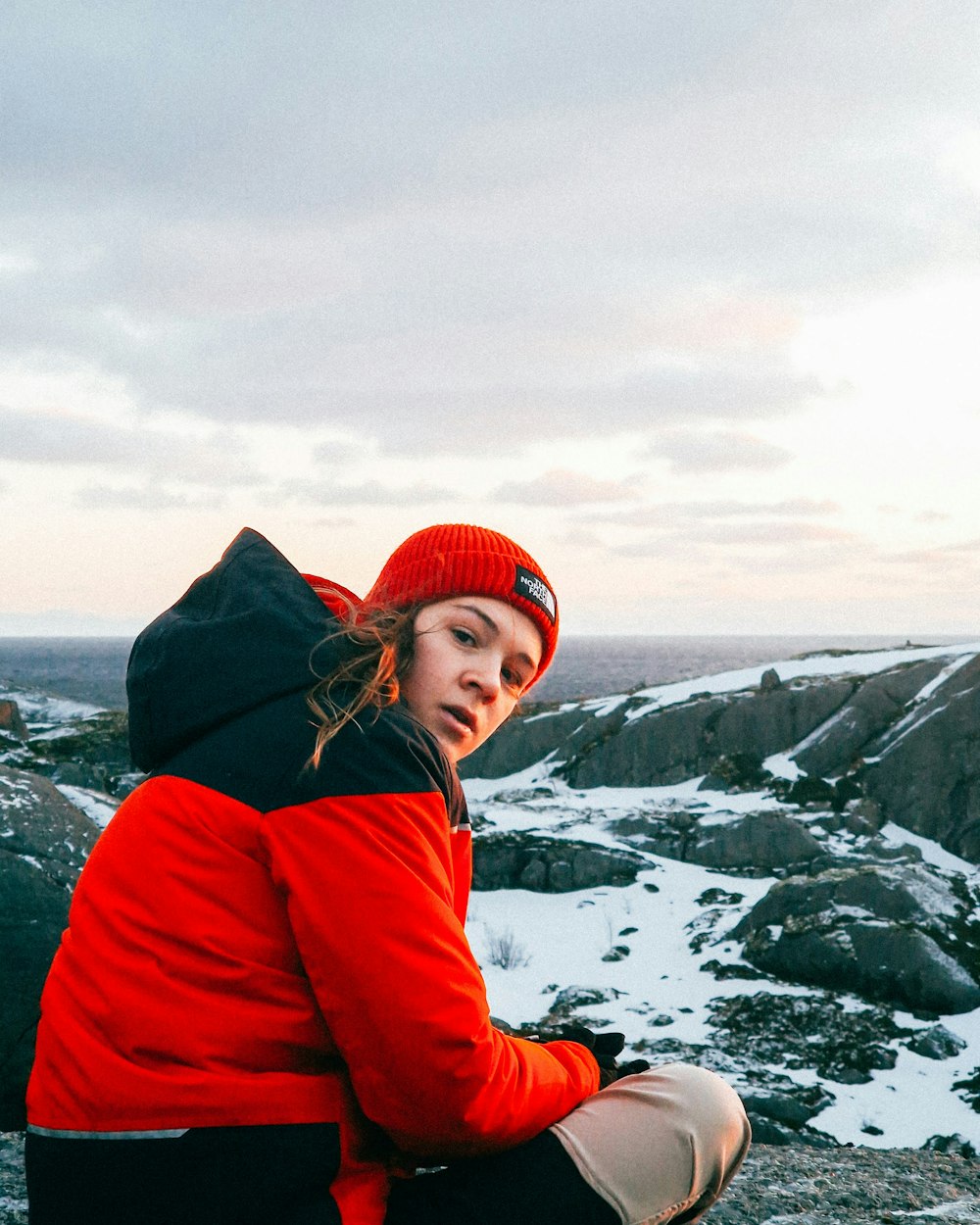 uma mulher sentada no topo de uma montanha coberta de neve