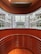 An architectural view reveals a modern indoor space with curving walls and metal railings overlooking a large glass-covered atrium. The design features a balance of metal and wood elements, highlighted by natural light from the expansive windows.