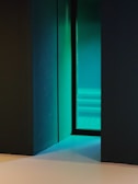 Minimalist shot of a darkened room with faint turquoise and violet reflections on textured surfaces.