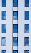 a tall white building with many windows reflecting the sky