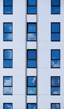 a tall white building with many windows reflecting the sky