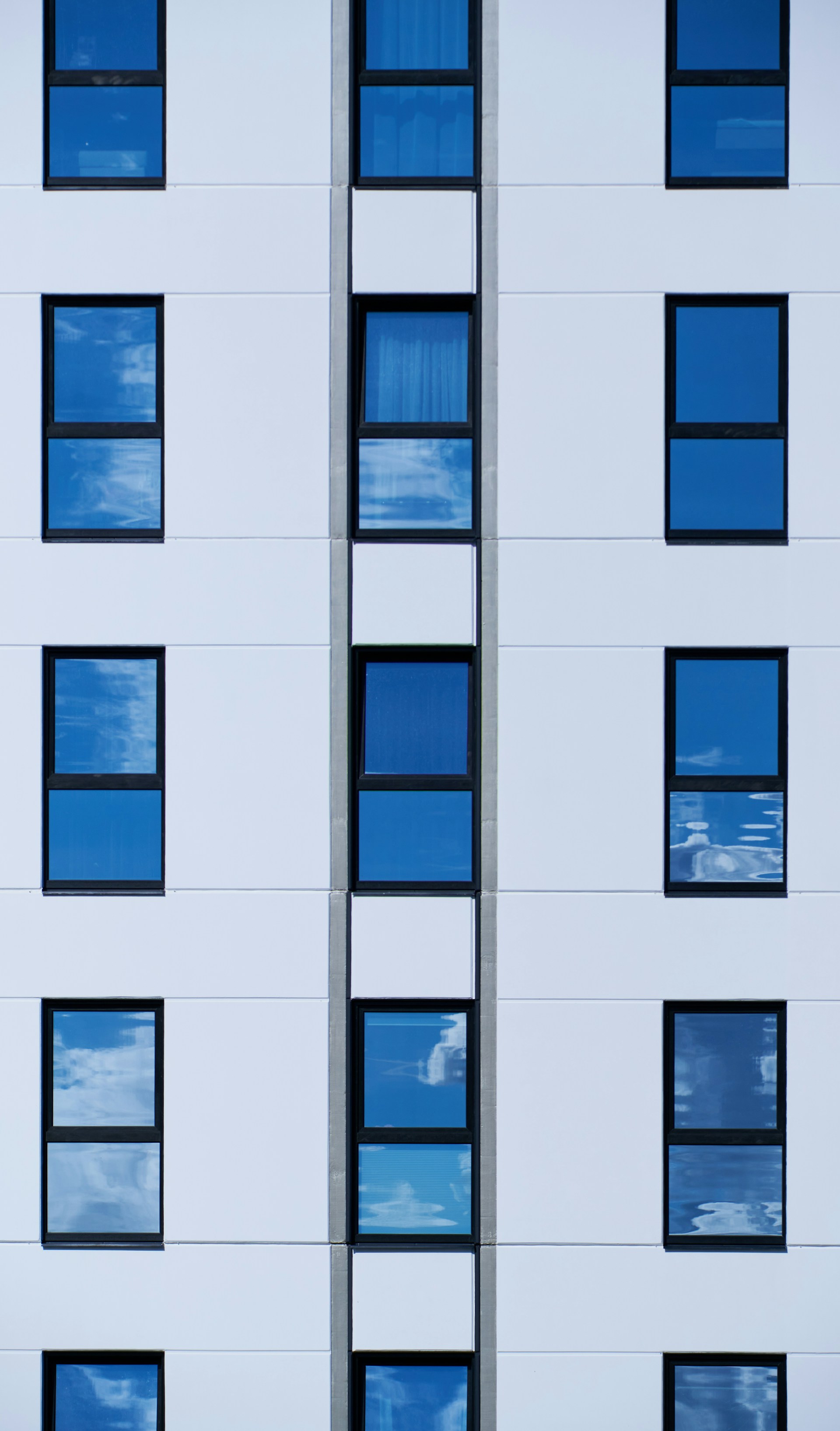 a tall white building with many windows reflecting the sky