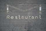 A textured gray wall with horizontal grooves has the word 'Restaurant' written on it in metallic letters.