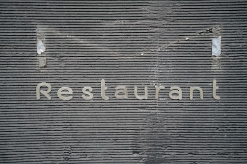 A textured gray wall with horizontal grooves has the word 'Restaurant' written on it in metallic letters.
