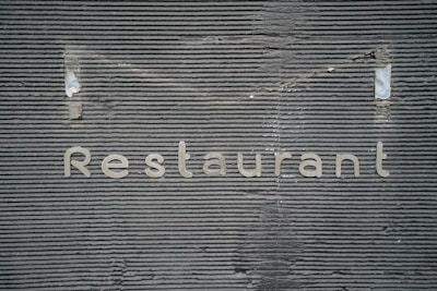 A textured gray wall with horizontal grooves has the word 'Restaurant' written on it in metallic letters.