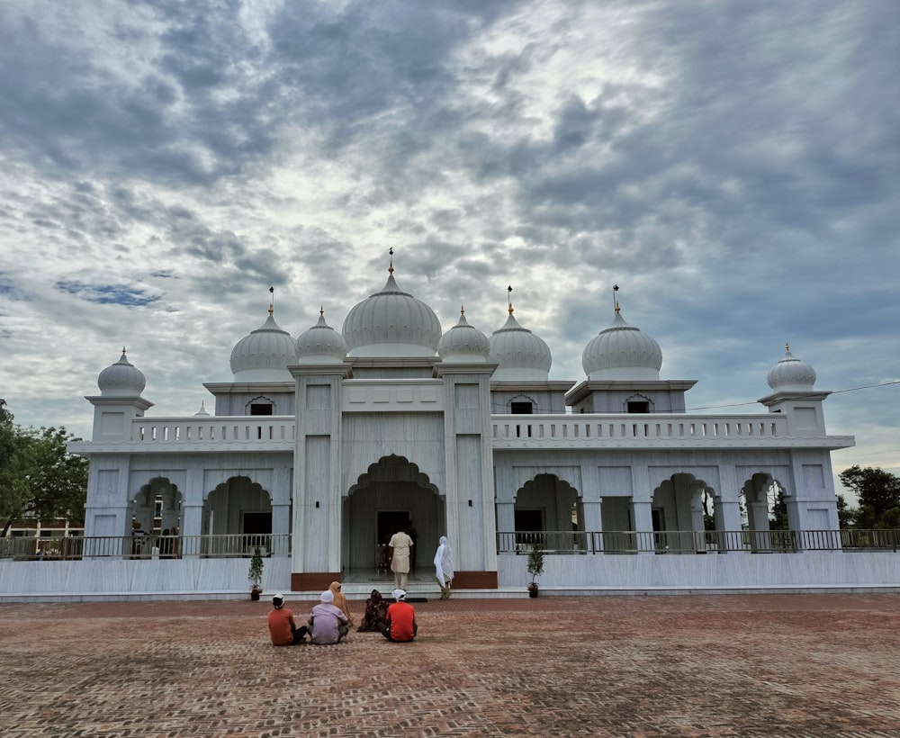 two people sitting on a bench in front of a white building