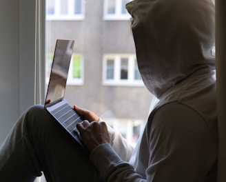 a person sitting on a window sill using a laptop