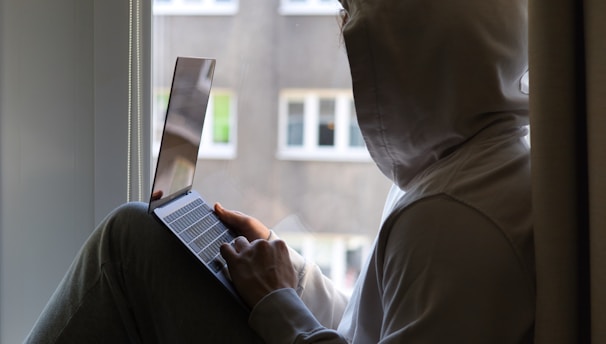 a person sitting on a window sill using a laptop