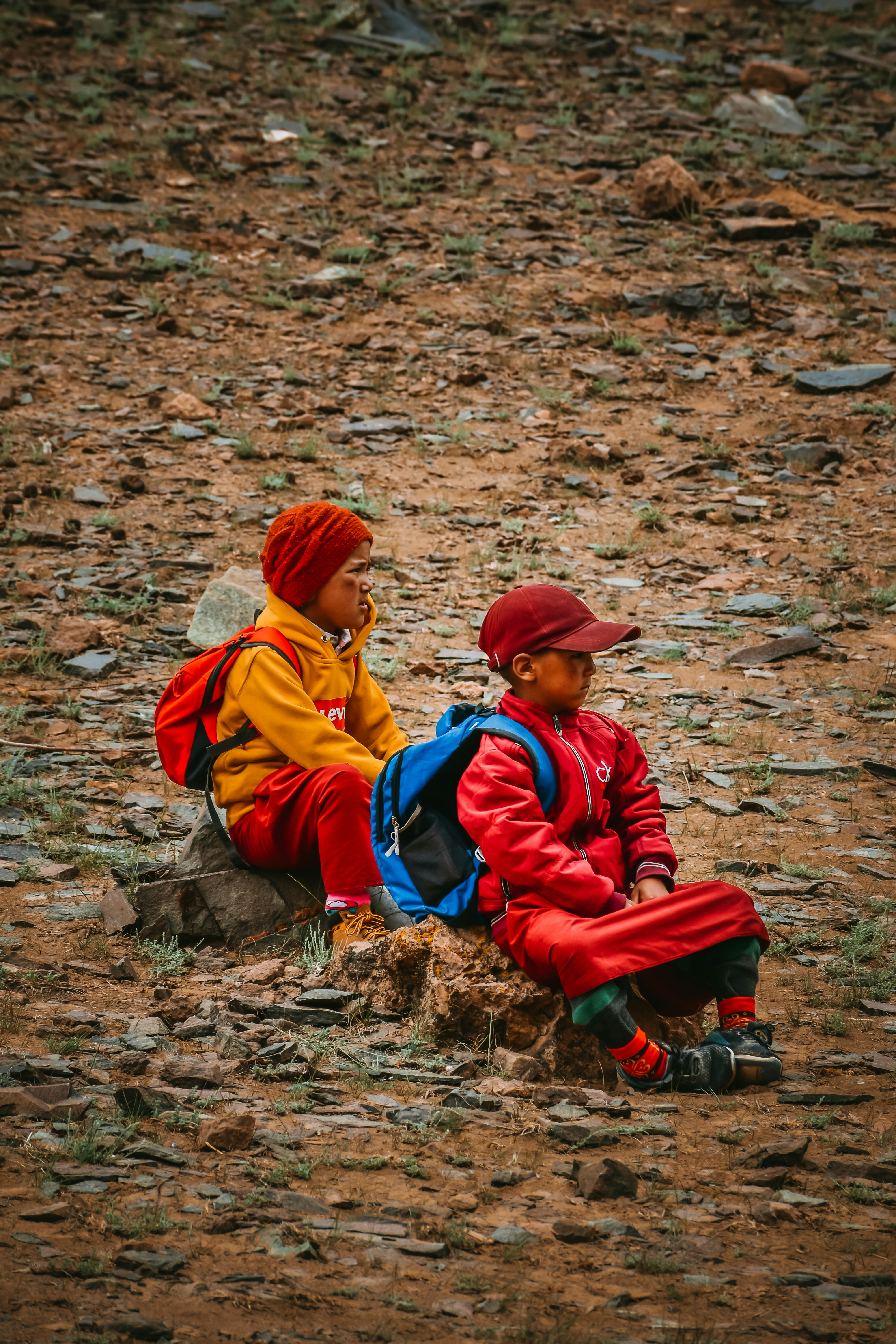 a couple of kids sitting on top of a dirt field