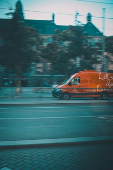 a red van driving down a street next to a tall building