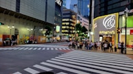 Colorful storefronts and pedestrians animatedly crossing a busy urban intersection.