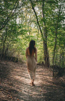 A woman walking barefoot on a forest path, sunlight filtering through the trees overhead.