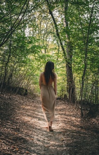An adult walking barefoot along a sunlit forest path, the earth visible beneath their feet.
