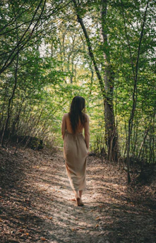 A joyful woman walking barefoot through a sunlit forest, embodying freedom and healing.