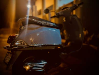 Evening lights reflecting off a parked TVS Jupiter scooter near the bustling Puri market street.
