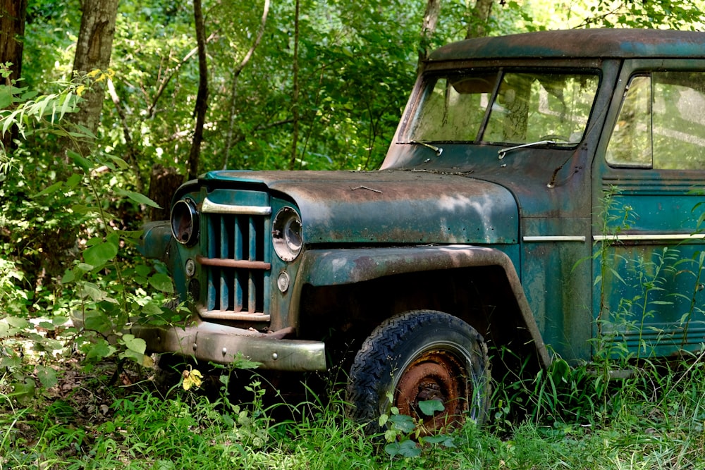 an old green truck sitting in the middle of a forest