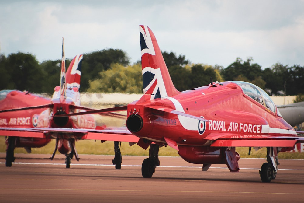 two red fighter jets sitting on top of an airport runway