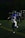 A person in a blue football uniform is running on a field. The player is wearing a helmet with a face guard. Other players and a referee can be seen in the background, all involved in an outdoor sports event during nighttime.