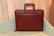 Elegant leather briefcase resting beside a vintage watch and notebook on a rich espresso brown surface.