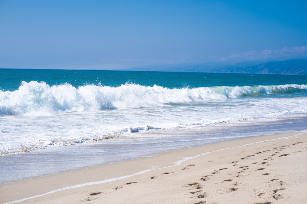 a sandy beach with a wave coming in and footprints in the sand