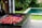 A luxurious spa setting featuring a bathtub filled with vibrant flower petals, arranged in an intricate pattern. The bathtub is situated in an open space with a view of a lush garden and a swimming pool surrounded by greenery. The area exudes a sense of tranquility and relaxation.
