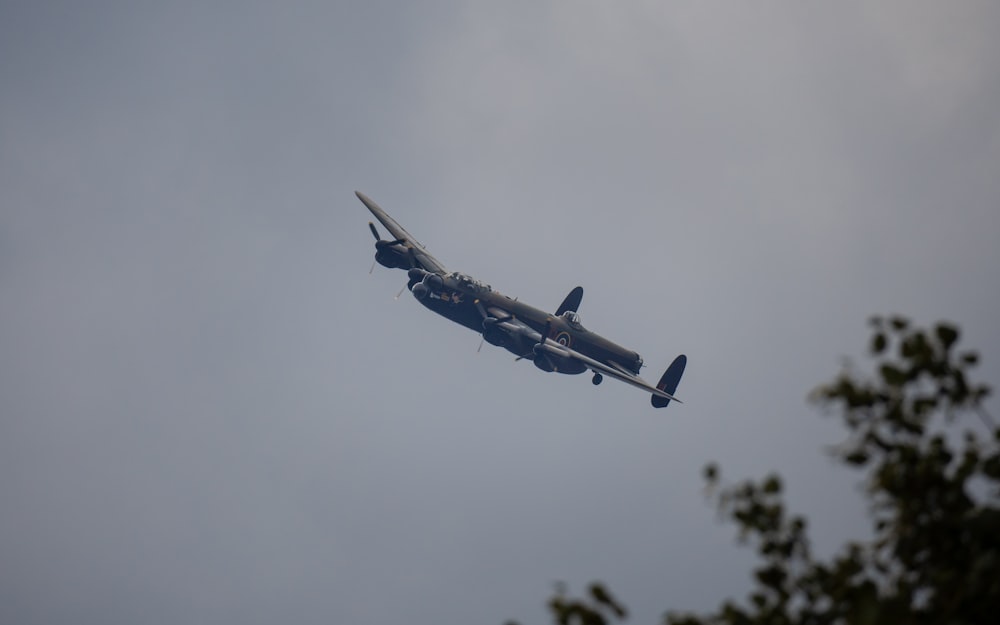 a plane flying in the sky with trees in the foreground