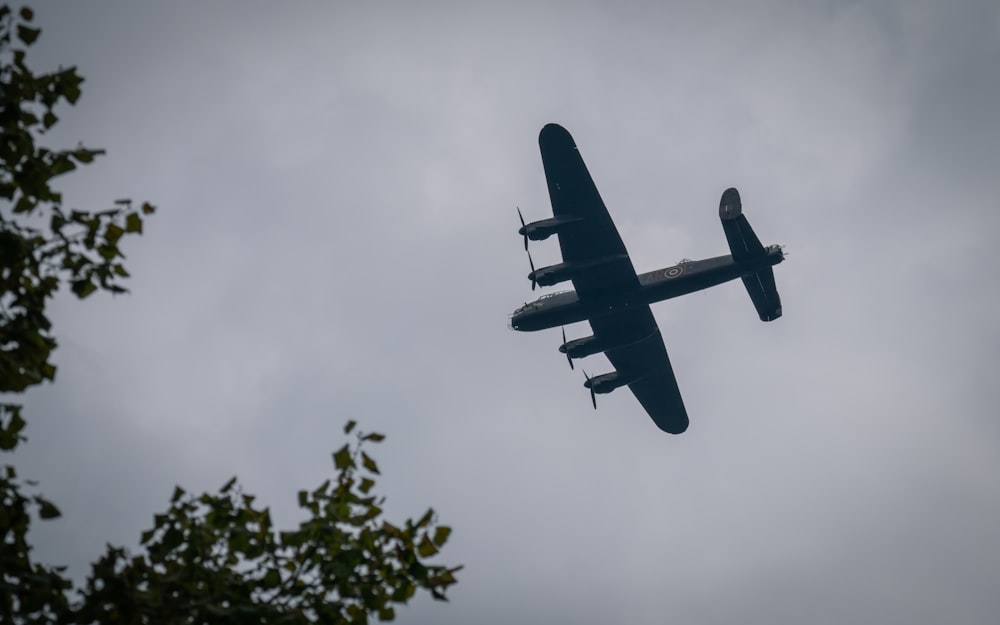 a plane flying in the sky with trees in the foreground