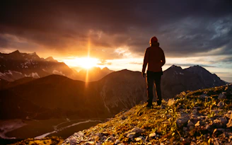 A vibrant photo of a traveler standing on a mountain peak at sunrise, overlooking a vast landscape.