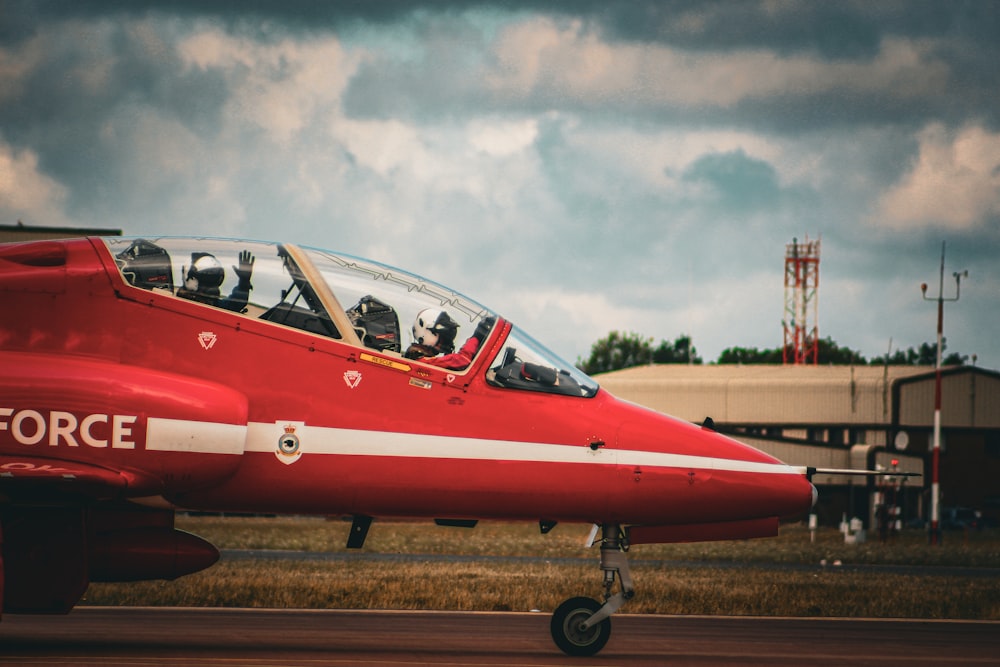 a red fighter jet sitting on top of an airport tarmac