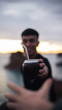Artisan pouring fresh mate tea into traditional cups outdoors in a green setting.