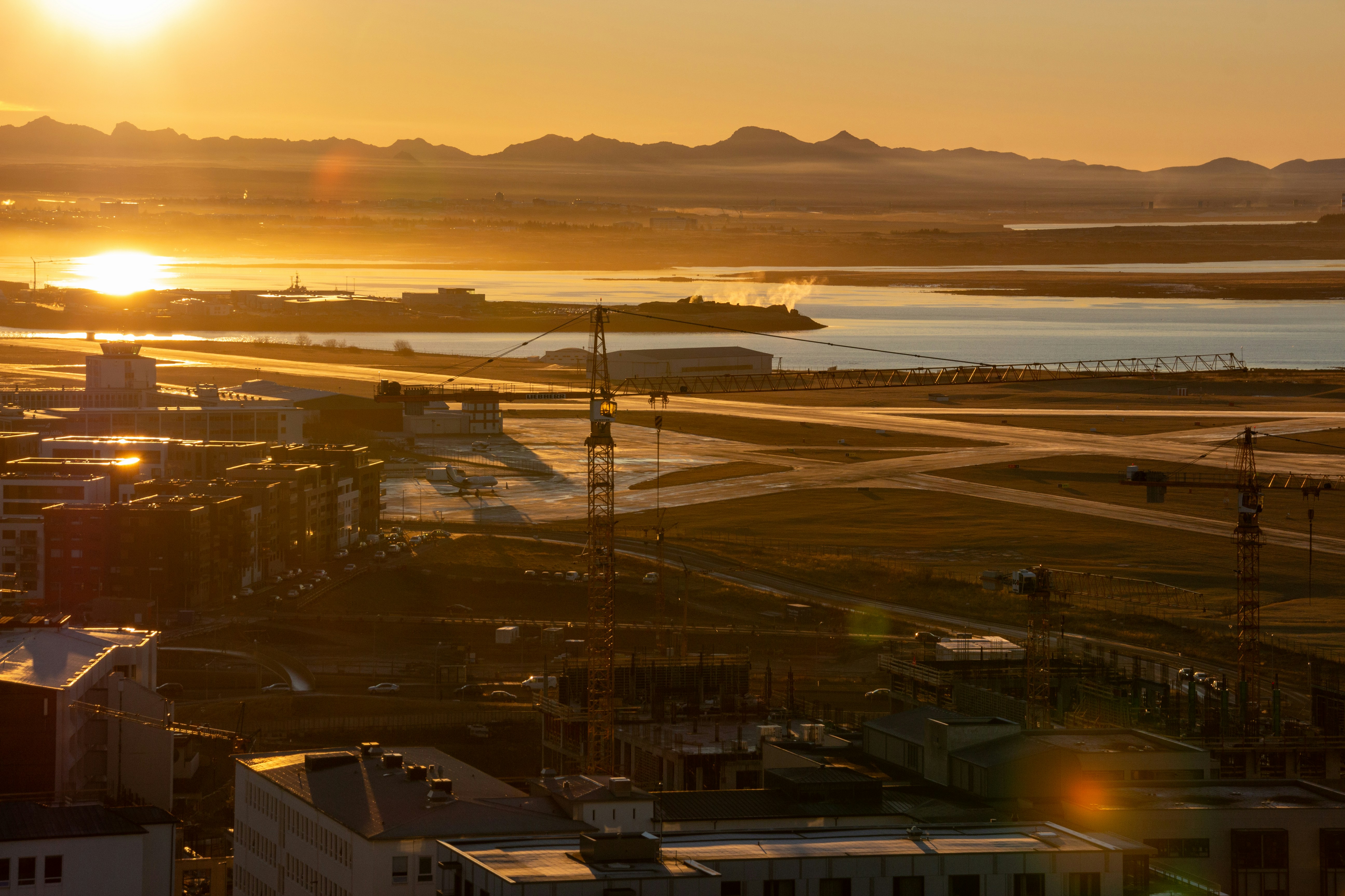 the sun is setting over a city with a body of water, 