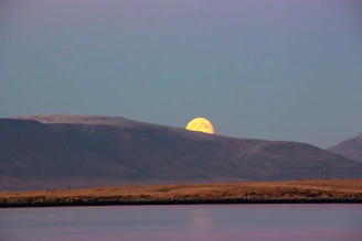 A glowing full moon rising over a calm lake at night.