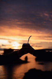a person holding a cell phone in front of a sunset