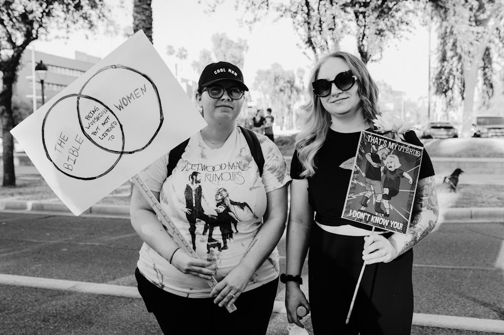 two women standing next to each other holding signs