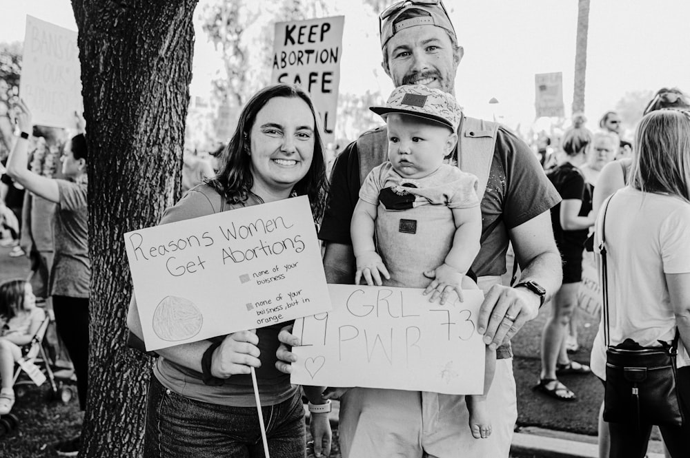 a man and woman holding a baby and a sign