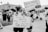 A black and white photo captures a group of people participating in a protest or demonstration. Two individuals in the foreground, an adult and a child, hold signs with messages advocating for women's rights and bodily autonomy. The background shows other participants holding similar protest signs, with trees and a building visible.