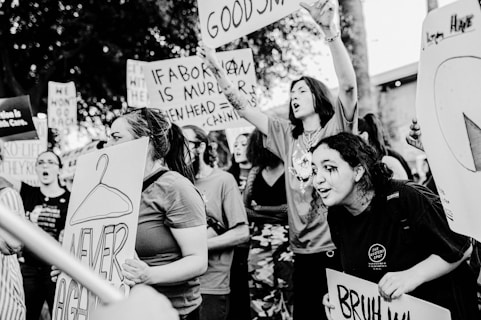 A group of people participate in a protest carrying various signs with messages related to abortion rights. The scene is dynamic, with individuals expressing strong emotions and engagement as they hold signs and chant.