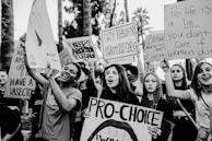 A group of people are gathered holding various pro-choice signs advocating for abortion rights. The signs contain messages such as 'Keep Abortion Legal' and 'Pro-Choice.' The scene appears to be a protest or demonstration, with individuals expressing strong emotions and determination.