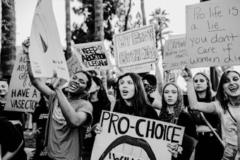 A group of people are gathered holding various pro-choice signs advocating for abortion rights. The signs contain messages such as 'Keep Abortion Legal' and 'Pro-Choice.' The scene appears to be a protest or demonstration, with individuals expressing strong emotions and determination.