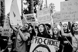 A group of people are gathered holding various pro-choice signs advocating for abortion rights. The signs contain messages such as 'Keep Abortion Legal' and 'Pro-Choice.' The scene appears to be a protest or demonstration, with individuals expressing strong emotions and determination.
