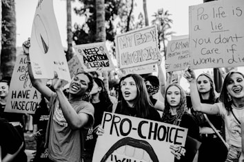 A group of people are gathered holding various pro-choice signs advocating for abortion rights. The signs contain messages such as 'Keep Abortion Legal' and 'Pro-Choice.' The scene appears to be a protest or demonstration, with individuals expressing strong emotions and determination.
