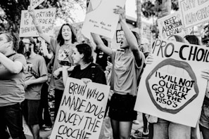 A group of people are actively participating in a protest, holding various signs and banners with slogans related to pro-choice and abortion rights. The scene is dynamic, with individuals expressing strong emotions and displaying a sense of unity and activism.